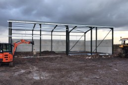 An in progress photograph of a steel portal framed building with concrete stock panels installed to the rear and side