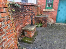 The brick-built well and copper to the rear of the Breach House. The brick boundary wall curves around the well.